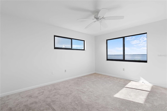 carpeted spare room with ceiling fan and a water view