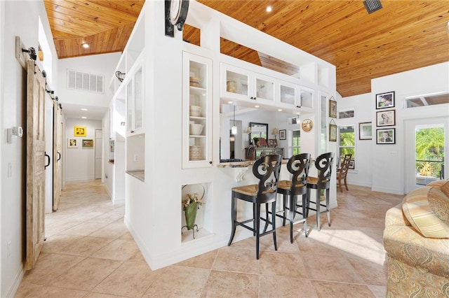 kitchen featuring wood ceiling, a breakfast bar area, white cabinets, a barn door, and light tile patterned floors