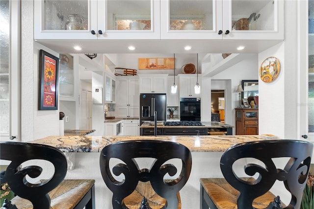 kitchen with pendant lighting, black appliances, light stone counters, and a breakfast bar area