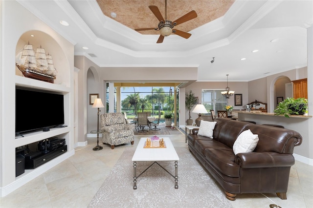 living room with a raised ceiling, built in features, ceiling fan with notable chandelier, and ornamental molding