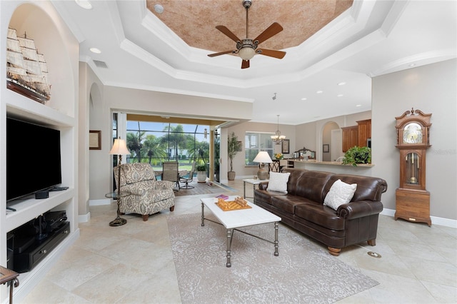 living room with a raised ceiling, built in shelves, crown molding, and ceiling fan with notable chandelier