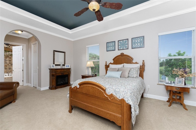 carpeted bedroom with ensuite bathroom, ceiling fan, crown molding, and a tray ceiling