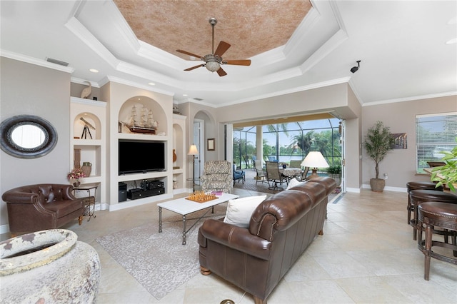 living room featuring a tray ceiling, built in shelves, crown molding, and ceiling fan