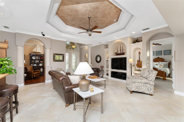 living room featuring built in shelves, ceiling fan, french doors, a raised ceiling, and ornamental molding