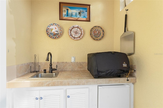 bar featuring white cabinets, tile counters, and sink