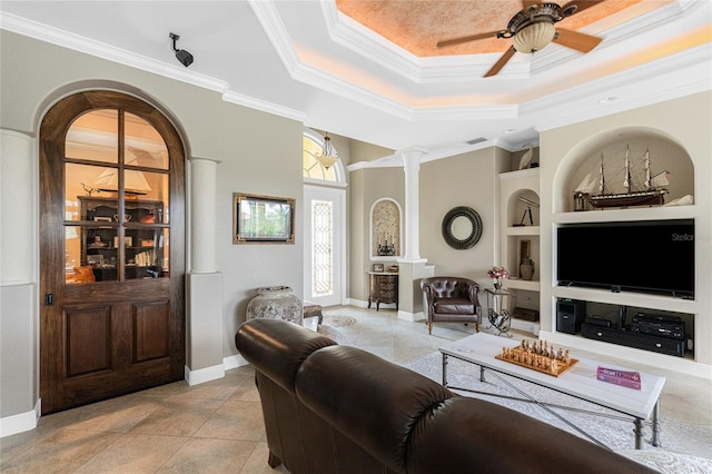 tiled living room featuring a raised ceiling, crown molding, built in shelves, ceiling fan, and decorative columns