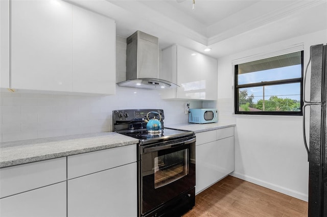 kitchen featuring baseboards, wall chimney exhaust hood, white cabinets, light wood-style flooring, and black appliances