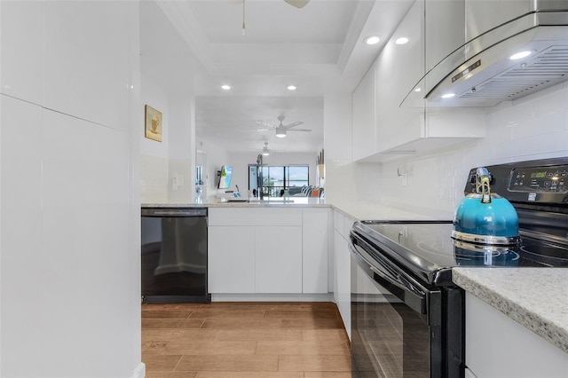 kitchen with ceiling fan, white cabinets, wall chimney exhaust hood, black appliances, and light wood-type flooring