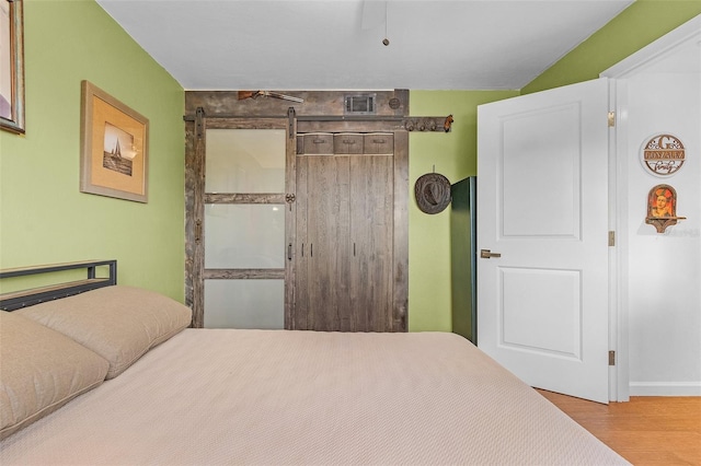 bedroom with a barn door and light hardwood / wood-style floors