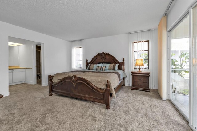 bedroom with a textured ceiling, light colored carpet, access to exterior, and ensuite bathroom