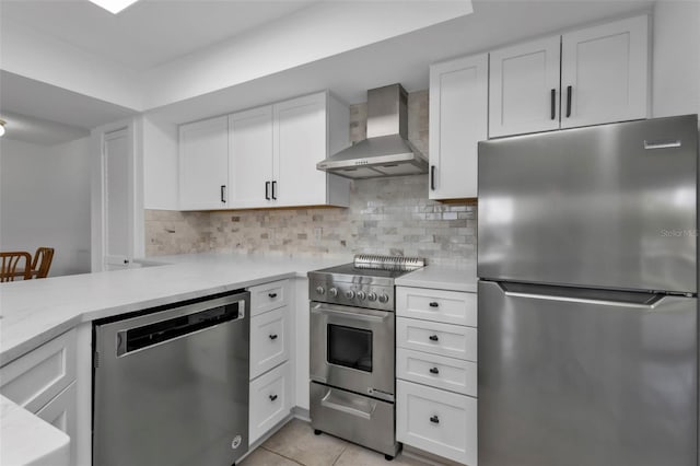 kitchen with white cabinetry, wall chimney exhaust hood, stainless steel appliances, decorative backsplash, and light tile patterned floors