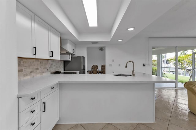 kitchen with white cabinetry, kitchen peninsula, a skylight, sink, and wall chimney range hood