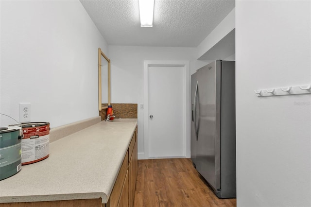 kitchen with a textured ceiling, light hardwood / wood-style flooring, sink, and stainless steel fridge with ice dispenser