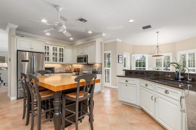 kitchen with pendant lighting, stainless steel appliances, sink, light tile patterned floors, and crown molding