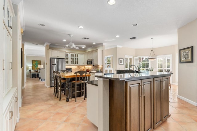 kitchen featuring stainless steel appliances, tasteful backsplash, hanging light fixtures, a kitchen island with sink, and cream cabinetry