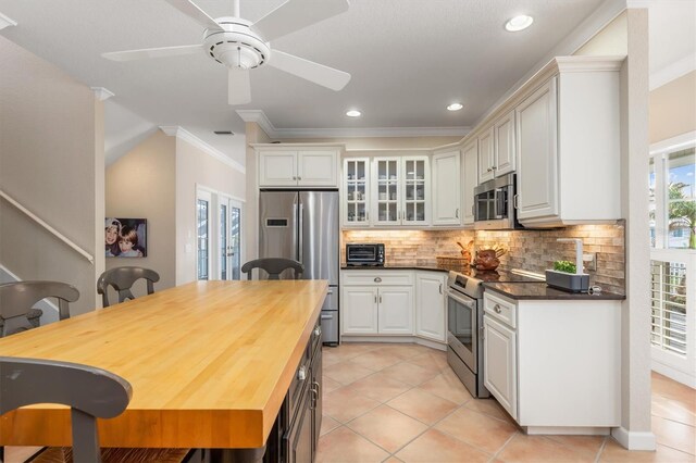 kitchen with white cabinetry, decorative backsplash, ornamental molding, wood counters, and stainless steel appliances