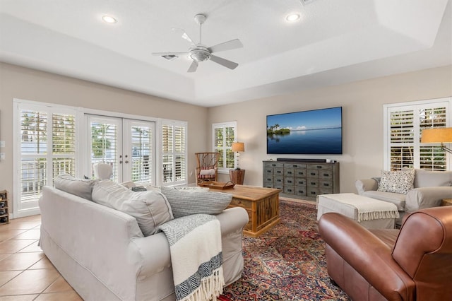 tiled living room with ceiling fan, french doors, and a raised ceiling