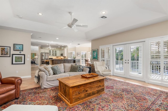 tiled living room with ceiling fan, a tray ceiling, and french doors