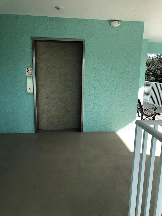 interior space featuring concrete flooring, a textured wall, and elevator