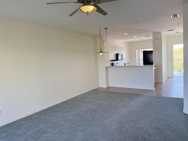 unfurnished living room with ceiling fan, light tile patterned floors, a textured ceiling, light carpet, and visible vents