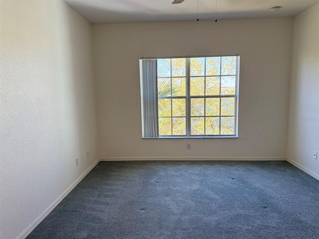 empty room featuring baseboards, dark carpet, and a ceiling fan