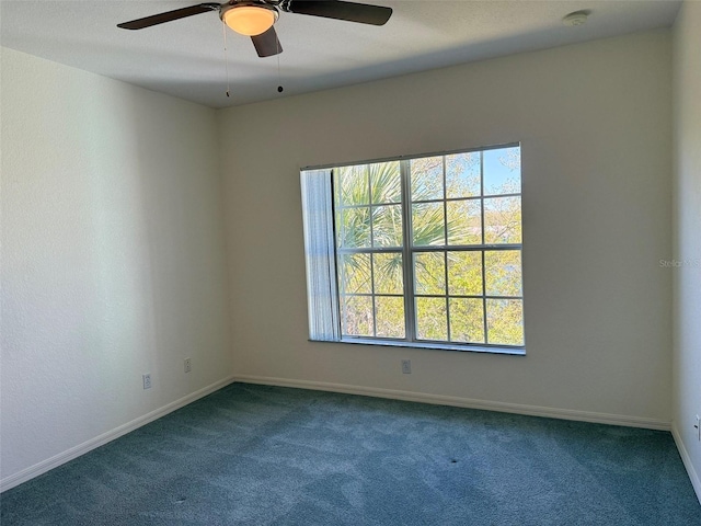 empty room with a ceiling fan, dark colored carpet, and baseboards