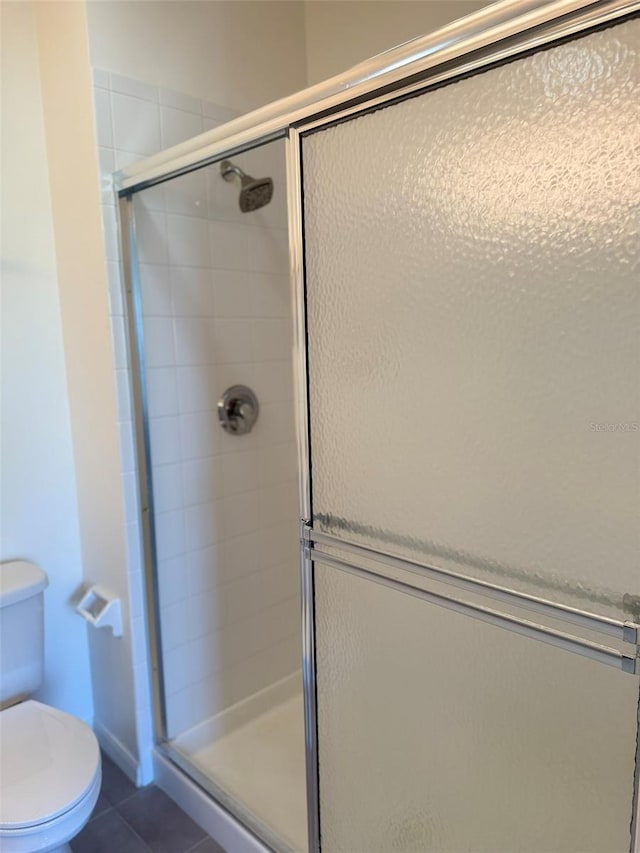 bathroom featuring toilet, a stall shower, and tile patterned floors