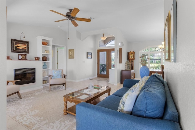 living room featuring ceiling fan with notable chandelier, built in shelves, vaulted ceiling, and light tile patterned floors