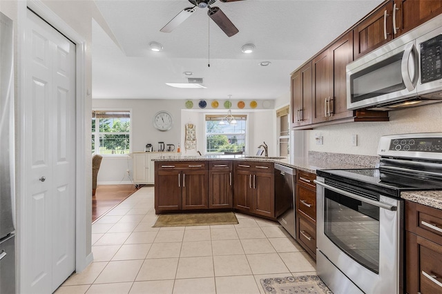 kitchen with ceiling fan, light tile patterned flooring, sink, stainless steel appliances, and light stone countertops