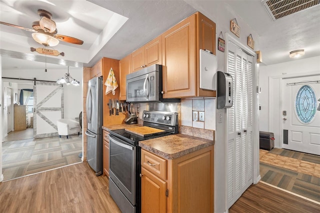 kitchen featuring appliances with stainless steel finishes, tasteful backsplash, a barn door, ceiling fan, and light hardwood / wood-style flooring