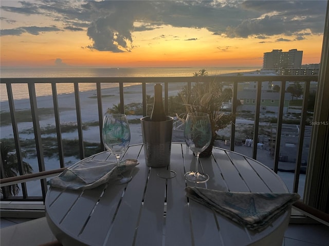 balcony at dusk featuring a water view and a view of the beach