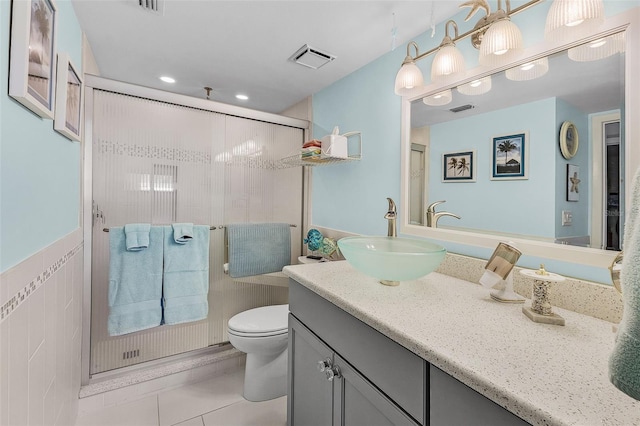 bathroom featuring a shower with door, tile walls, toilet, vanity, and tile patterned floors