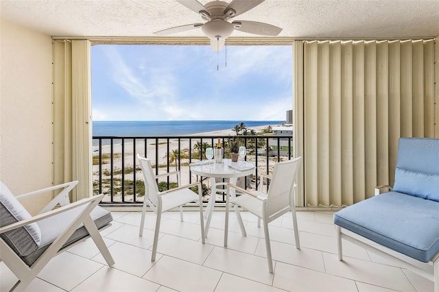 balcony with a water view, a beach view, and ceiling fan