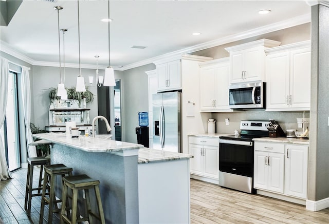 kitchen featuring a kitchen island with sink, stainless steel appliances, hanging light fixtures, and light hardwood / wood-style floors