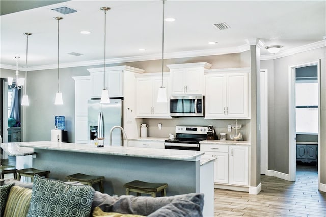 kitchen with an island with sink, white cabinets, stainless steel appliances, light wood-type flooring, and decorative light fixtures