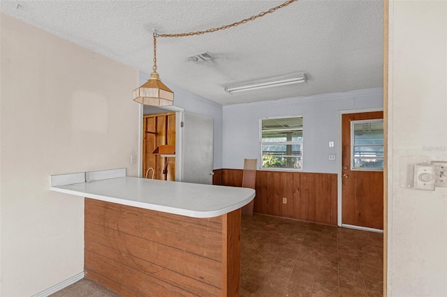 kitchen with kitchen peninsula, pendant lighting, a textured ceiling, and wooden walls