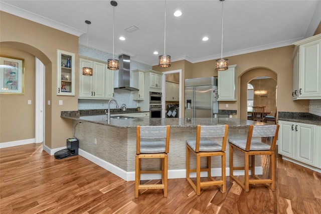 kitchen featuring dark stone countertops, wall chimney exhaust hood, hanging light fixtures, and appliances with stainless steel finishes