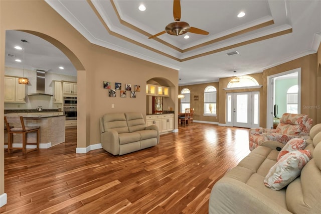 living room featuring ceiling fan, wood-type flooring, crown molding, and a tray ceiling