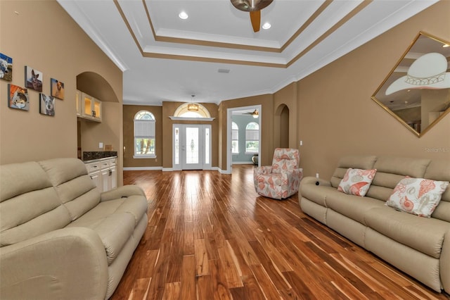 living room with hardwood / wood-style floors, ceiling fan, a raised ceiling, and ornamental molding