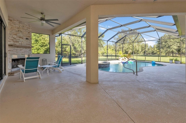 view of swimming pool featuring an outdoor stone fireplace, ceiling fan, glass enclosure, a yard, and a patio