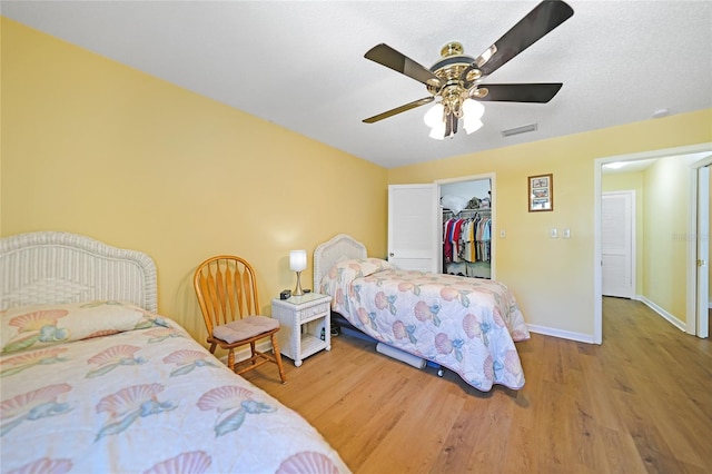 bedroom with wood-type flooring, a walk in closet, a closet, and ceiling fan