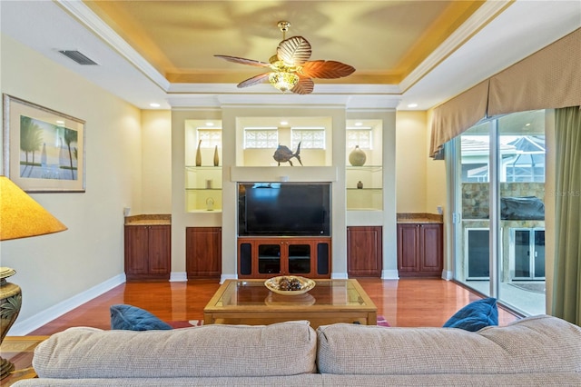 living room featuring wood-type flooring, a tray ceiling, ornamental molding, and ceiling fan