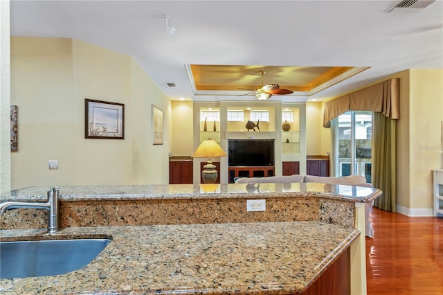 kitchen featuring ceiling fan, a raised ceiling, light stone counters, and hardwood / wood-style floors