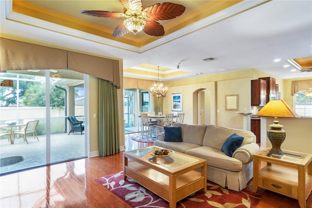 living room featuring wood-type flooring, ceiling fan with notable chandelier, a raised ceiling, and ornamental molding