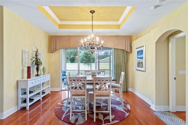 dining room featuring an inviting chandelier, hardwood / wood-style flooring, and a raised ceiling