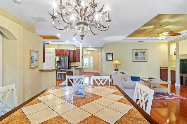 dining space with ceiling fan with notable chandelier, light wood-type flooring, and a raised ceiling