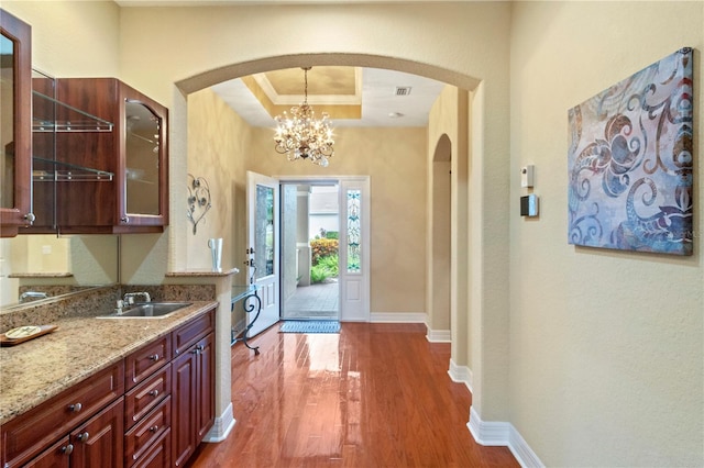 kitchen with light stone counters, hanging light fixtures, an inviting chandelier, a raised ceiling, and dark hardwood / wood-style flooring