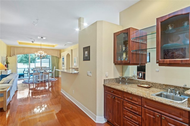 kitchen with hanging light fixtures, light stone countertops, light wood-type flooring, sink, and a notable chandelier