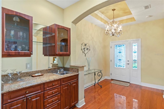 entrance foyer with a raised ceiling, light wood-type flooring, crown molding, sink, and a chandelier