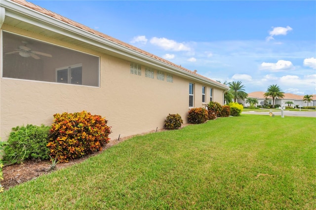 view of side of home with ceiling fan and a yard